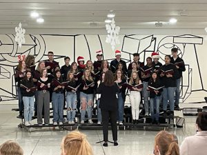 chorus singers some wearing holiday hats standing together ready to perform.