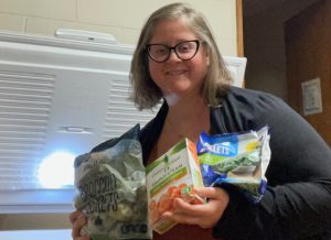 teacher stands holding a bunch of freezer food 