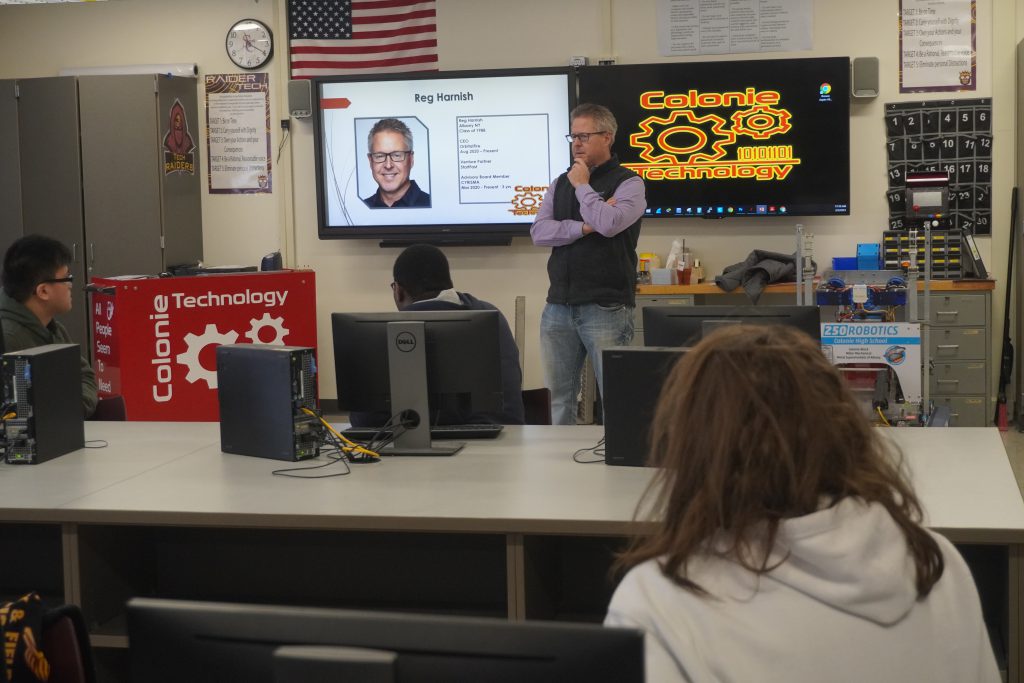 a man standing in front of a technology classroom engaging with students. 