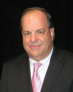 headshot of a man wearing a black suit with a black background