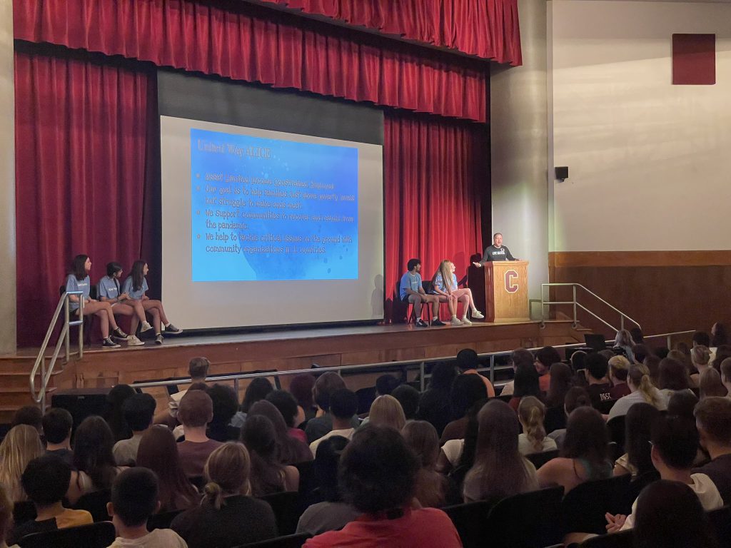 man speaks on stage, students are sitting on stage, students in the audience.