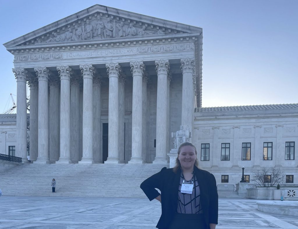 girl stands in front of supreme court building it says equal justice under law on the building.