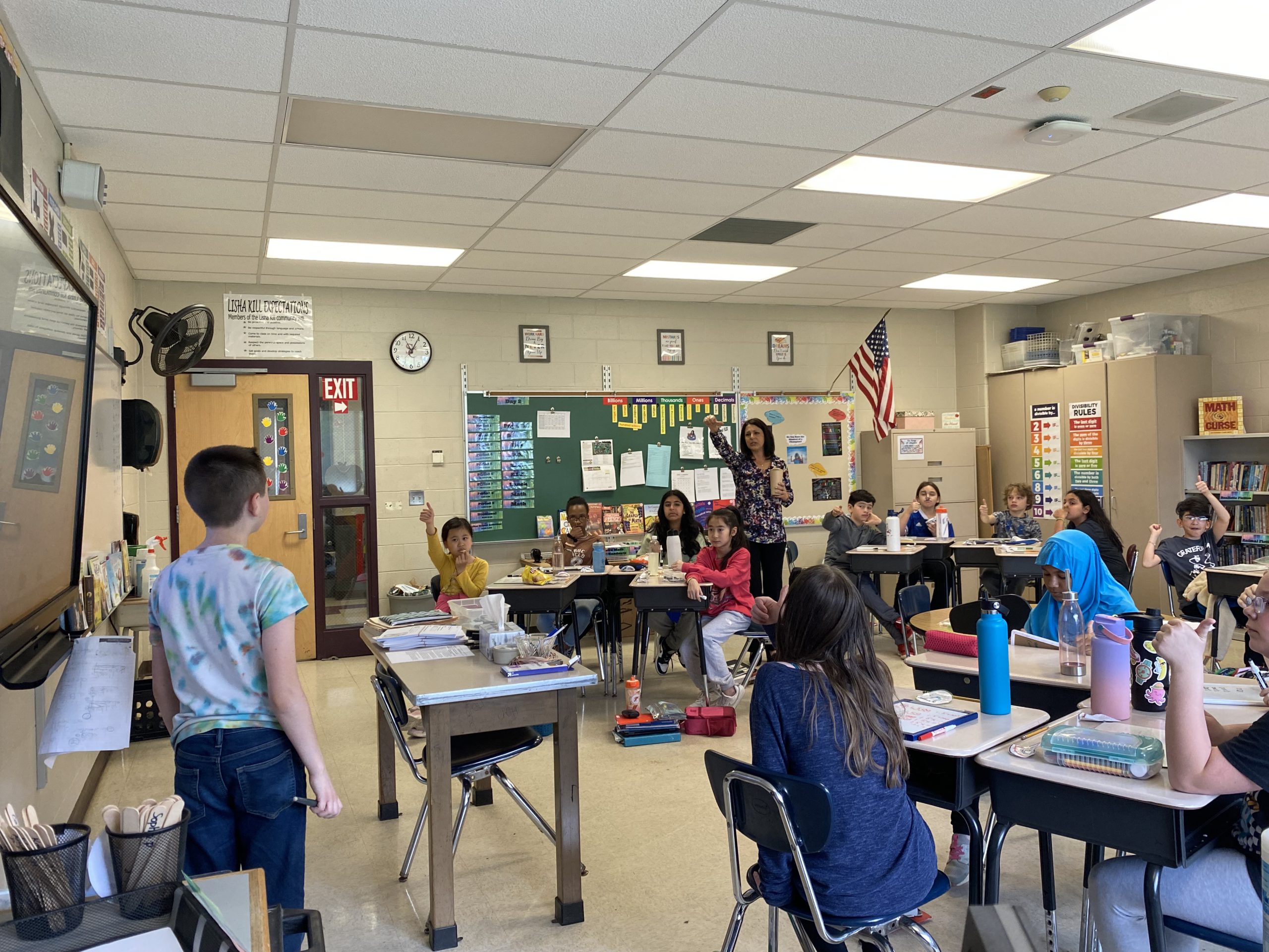 Student shows work on the board as classmates raise their hands to participate in the group activity