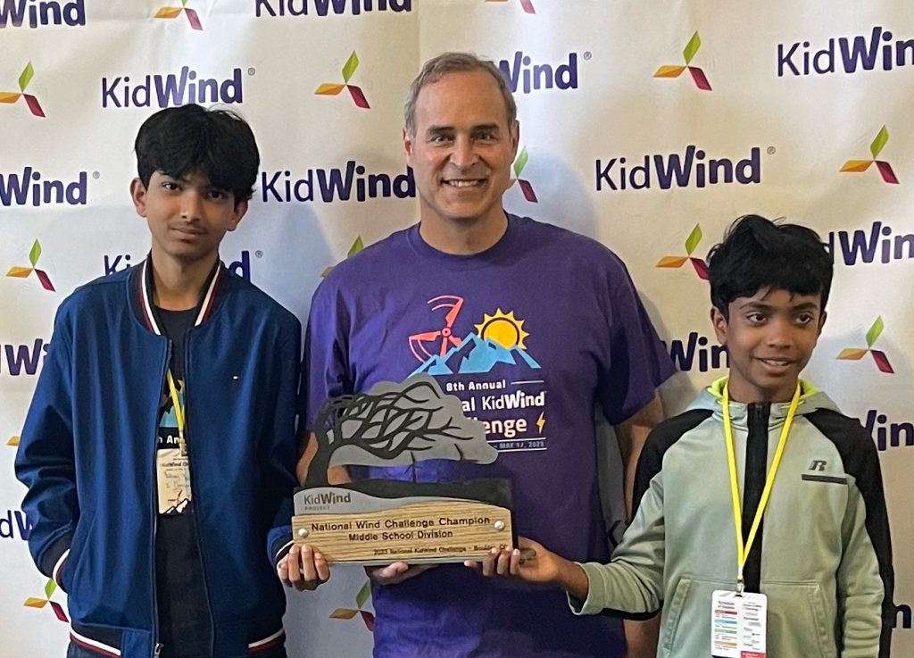 two students stand with the teacher holding the KidWind national championship trophy.