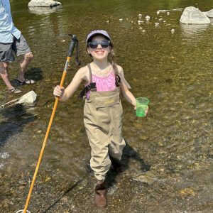 girl standing in the creek holding a cup