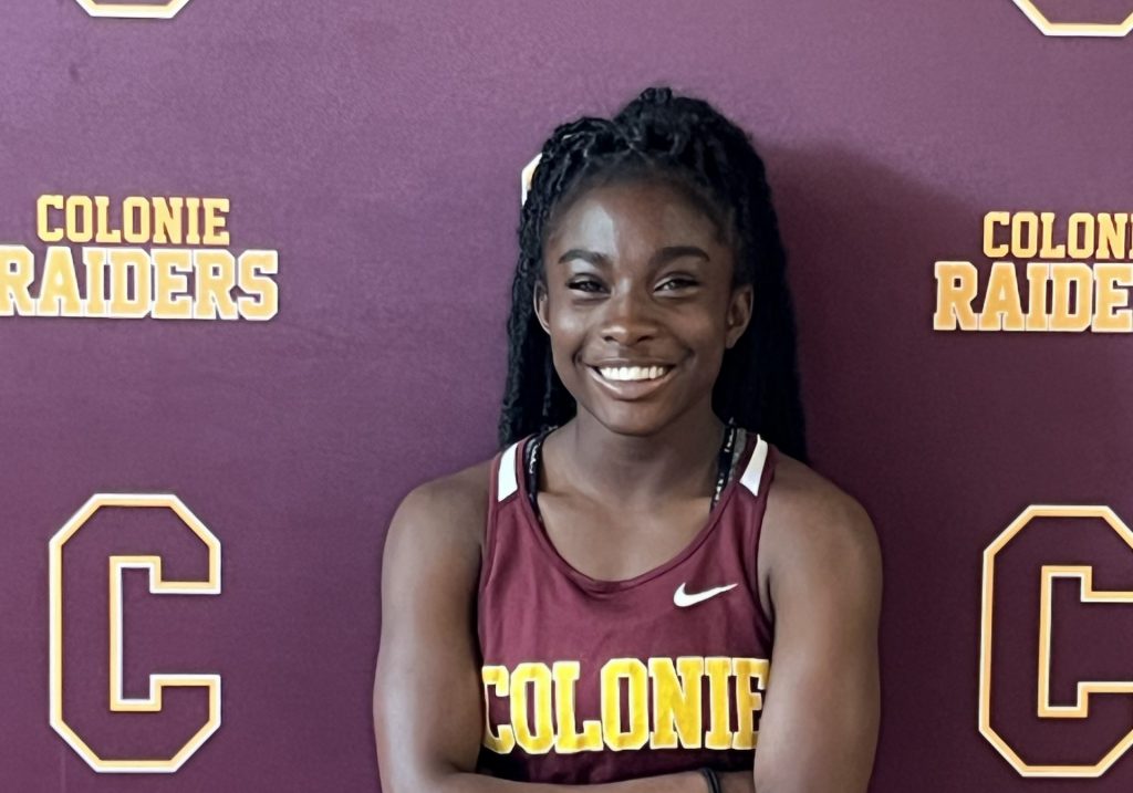 female track athlete posing in front of a backdrop that says Colonie Athletics.