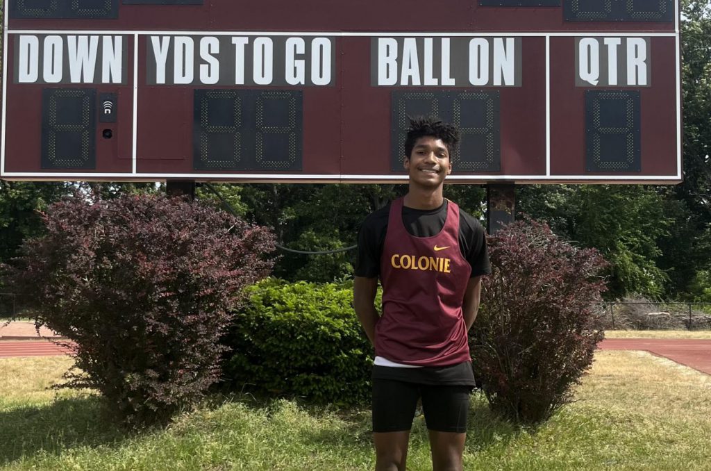 boys track athlete poses for a photo outside in front of the score board.