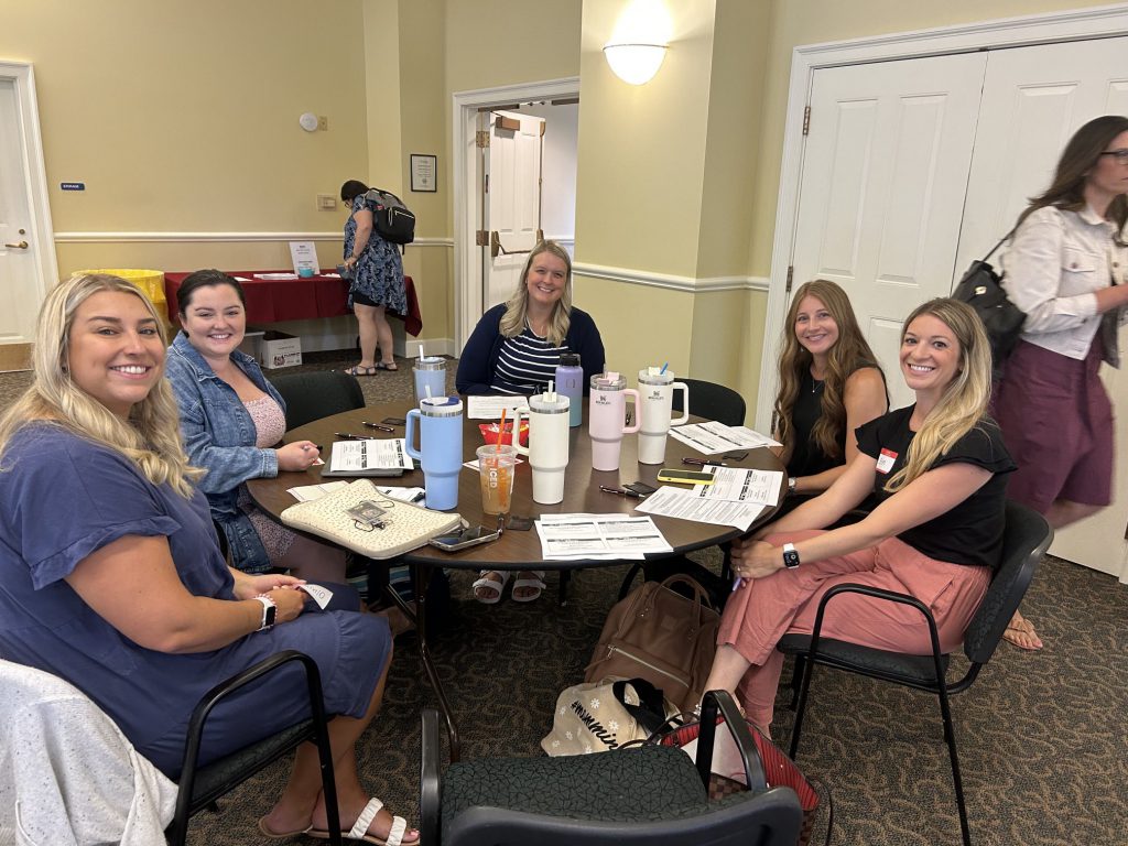 a group of five teachers pose for a photo at a table. 