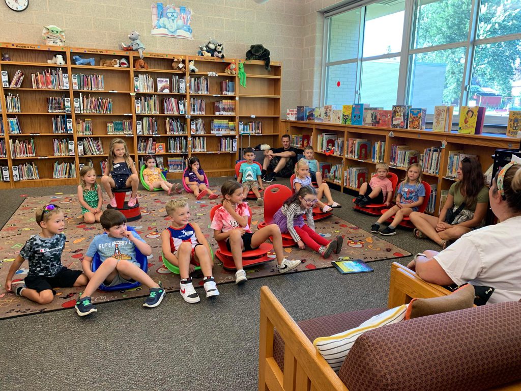 students and parents sit on the carpet in the library together