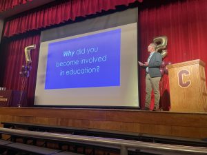 man presents on stage with screen behind him