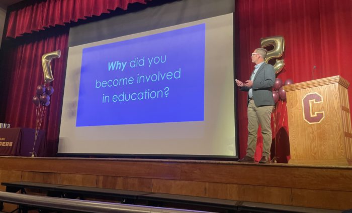 man presents on stage with screen behind him