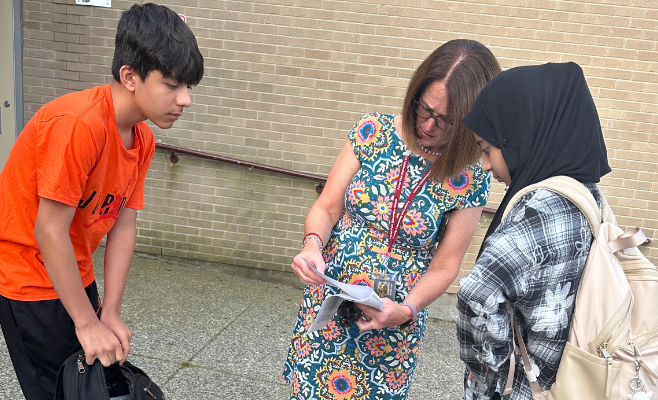 Female principal reads students schedule to help them find their way on the first day of school.