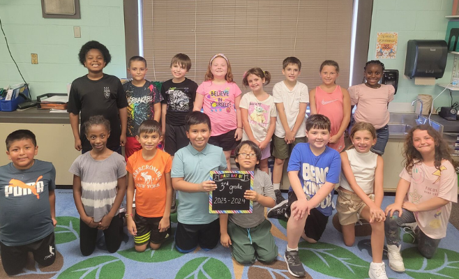 students pose for a photo holding a third grade sign.