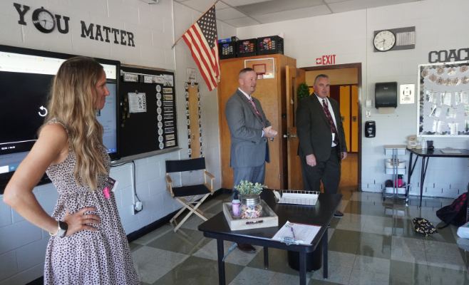 Principal, superintendent and teacher stand in classroom together.