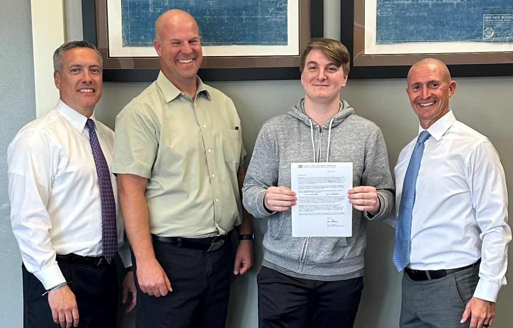 three men and one student stand and pose with letter.