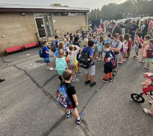 students stand outside of the school some with bikes and some without and talk to the principal.