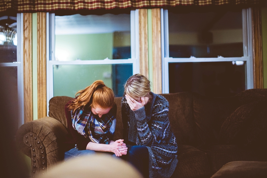 Two women grieving sitting on a couch holding hands