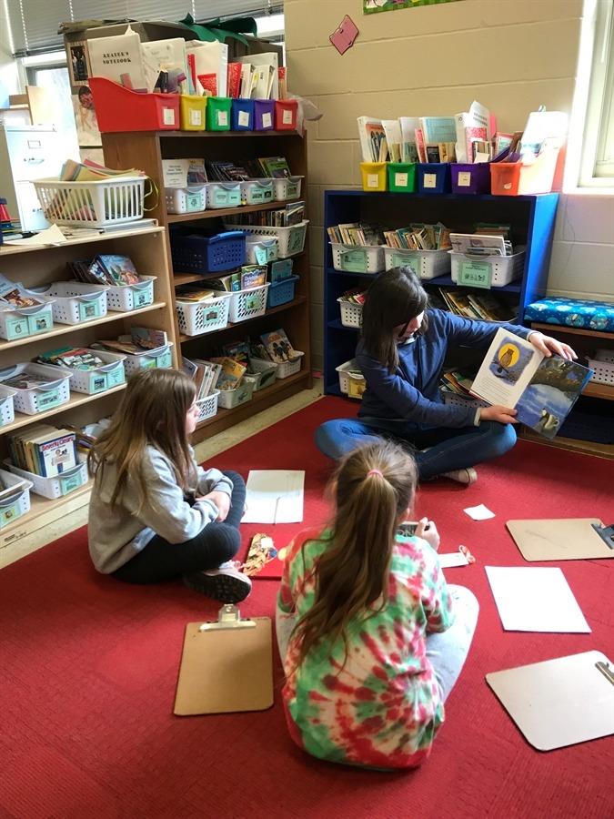 Classroom setting with three students reading and sharing books.