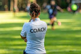 The back view of a female coach with a shirt that reads "COACH" on it.