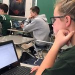 a student in a classroom sits at her desk and looks at her computer