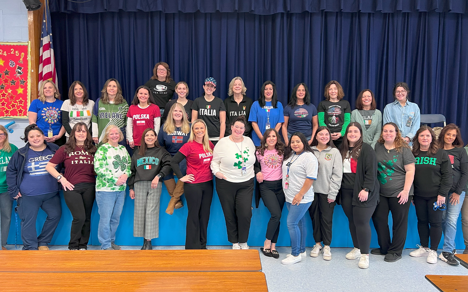 Many people near and on the stage dressed in Tshirts that say Irish, Italia, and many more cultures