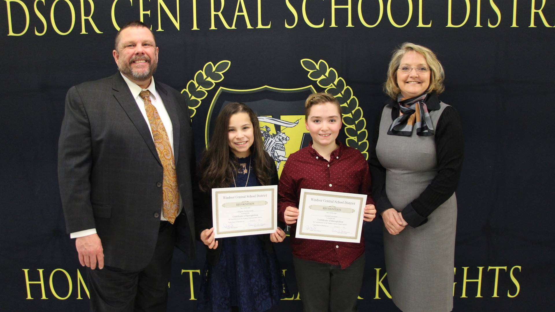 Two adults and two children standing in front of a Windsor schools black banner