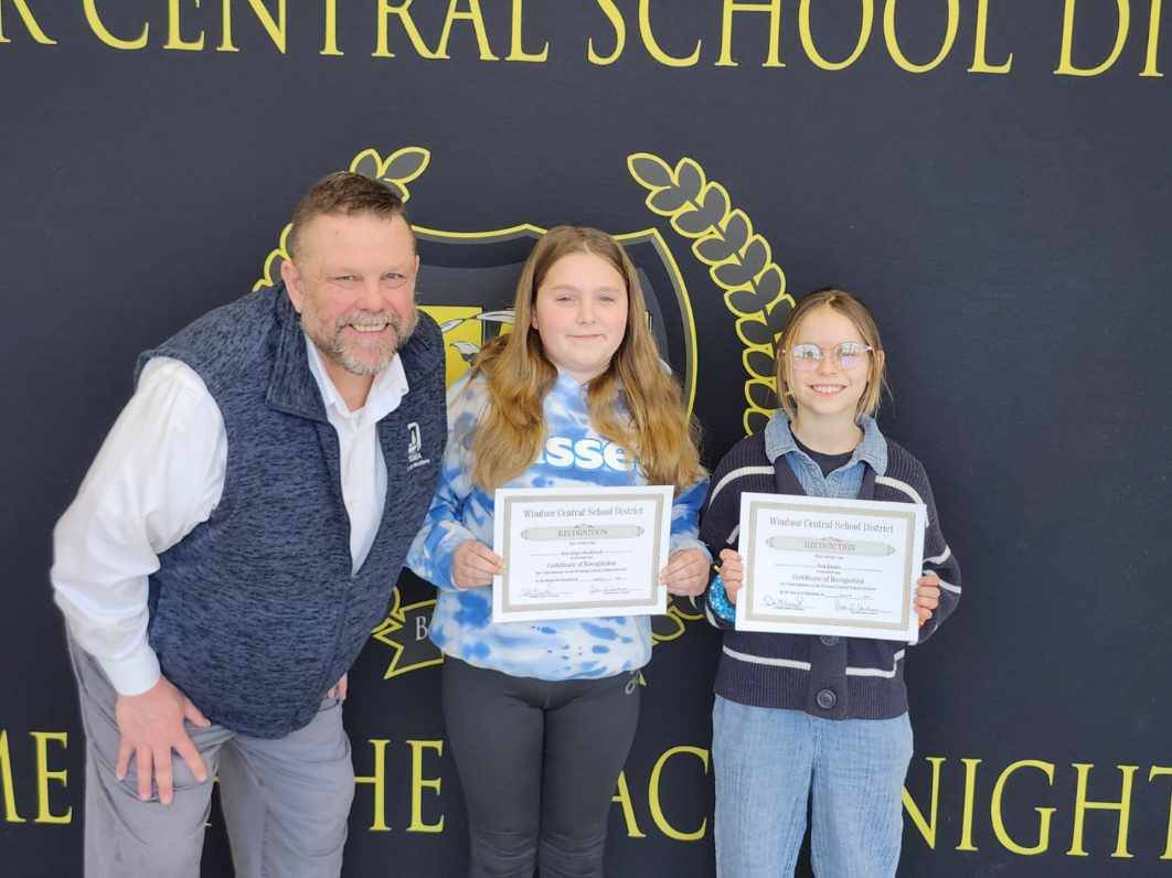 Pete Nowacki and two girls standing in front of a banner