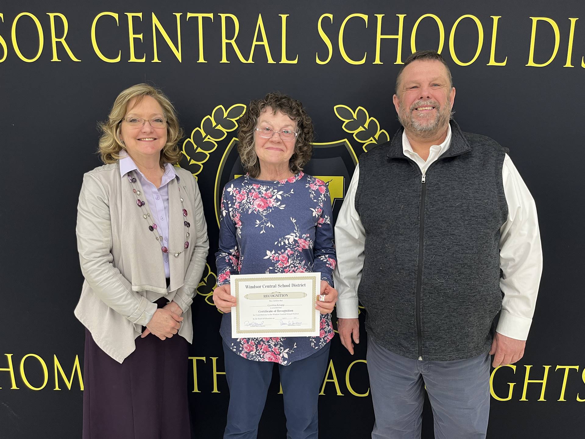 Margo Kibler, Cynthia (Nene) Knapp, and Pete Nowacki standing in front of a banner