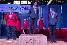 Jordan Mahar, in a red jacket, stands on a podium