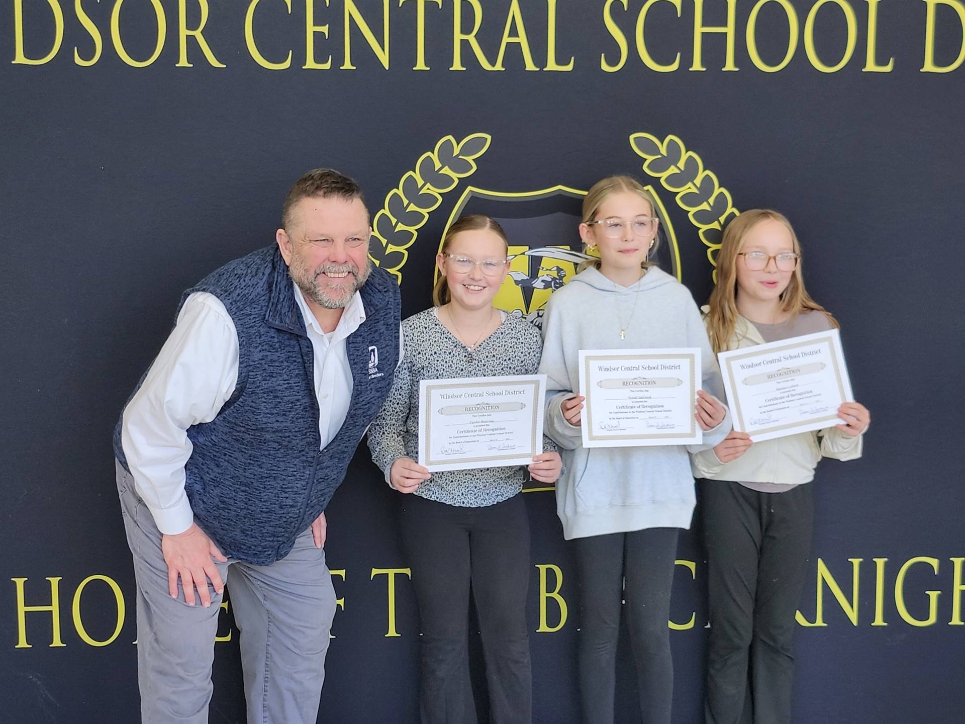 A man standing with three girls in front of a banner
