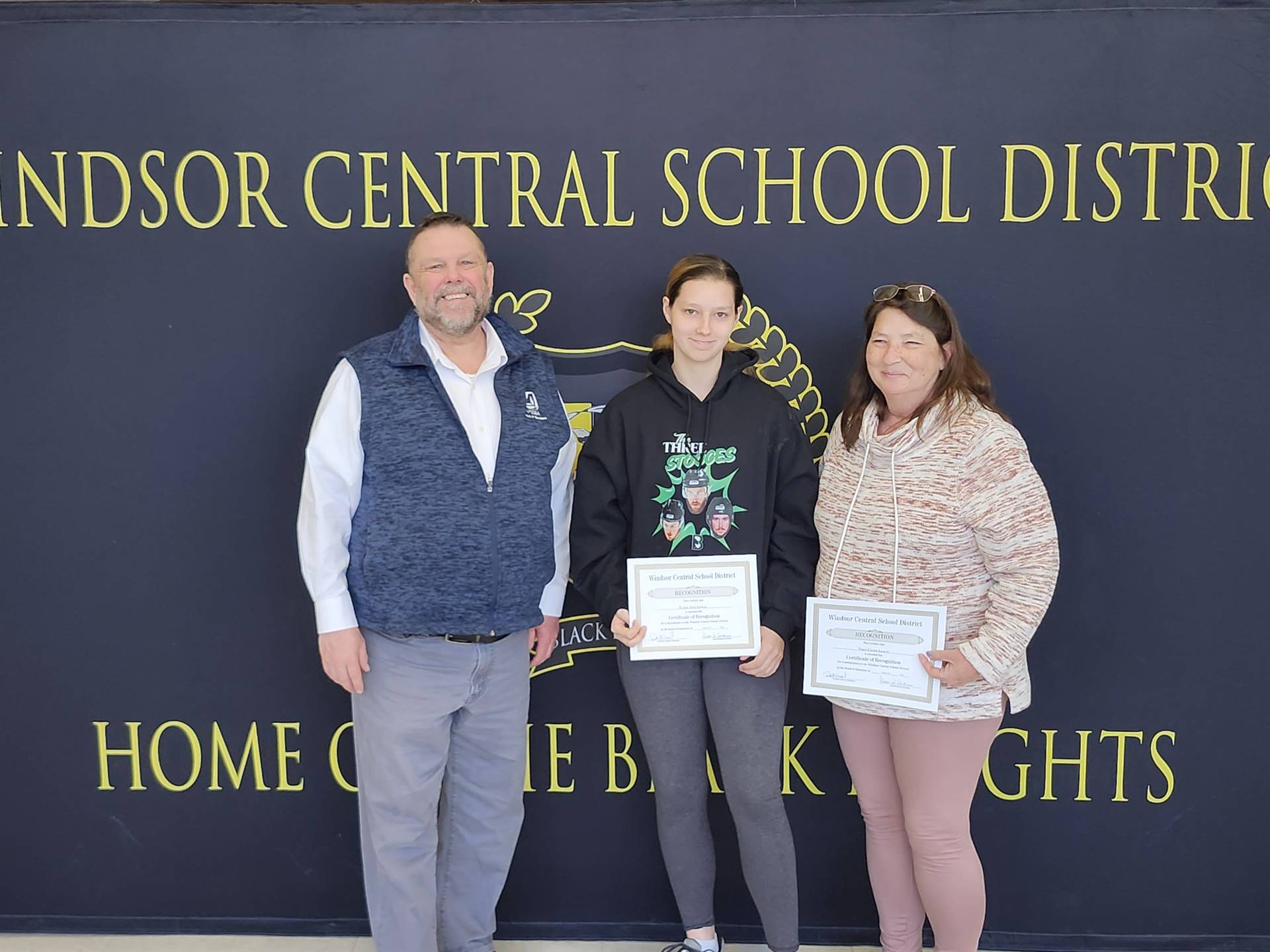 Pete Nowacki, Trista Ann Lewis, and Tracy Cross Lewis standing in front of a banner