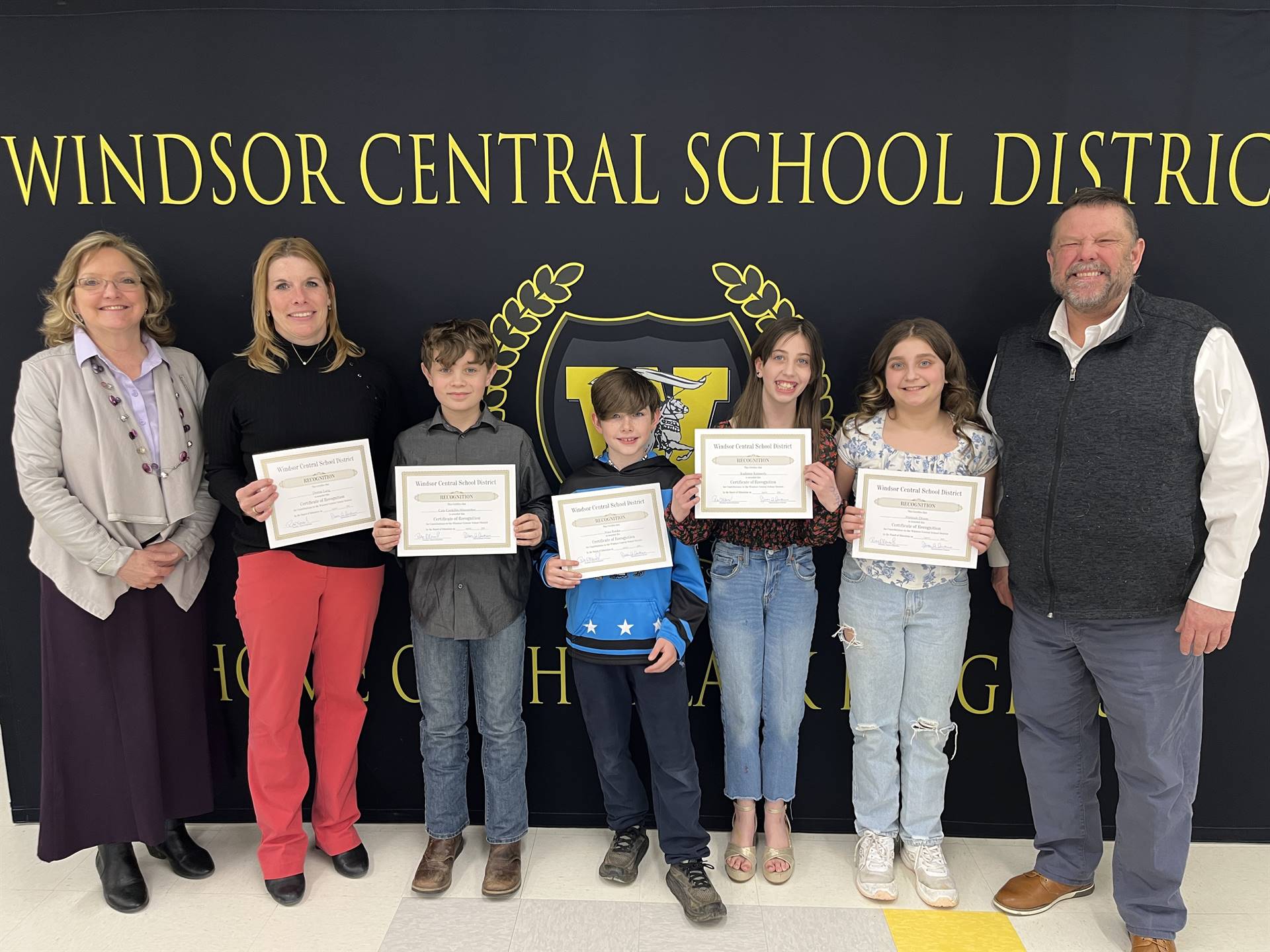 Four children standing between two women and a man in front of a banner