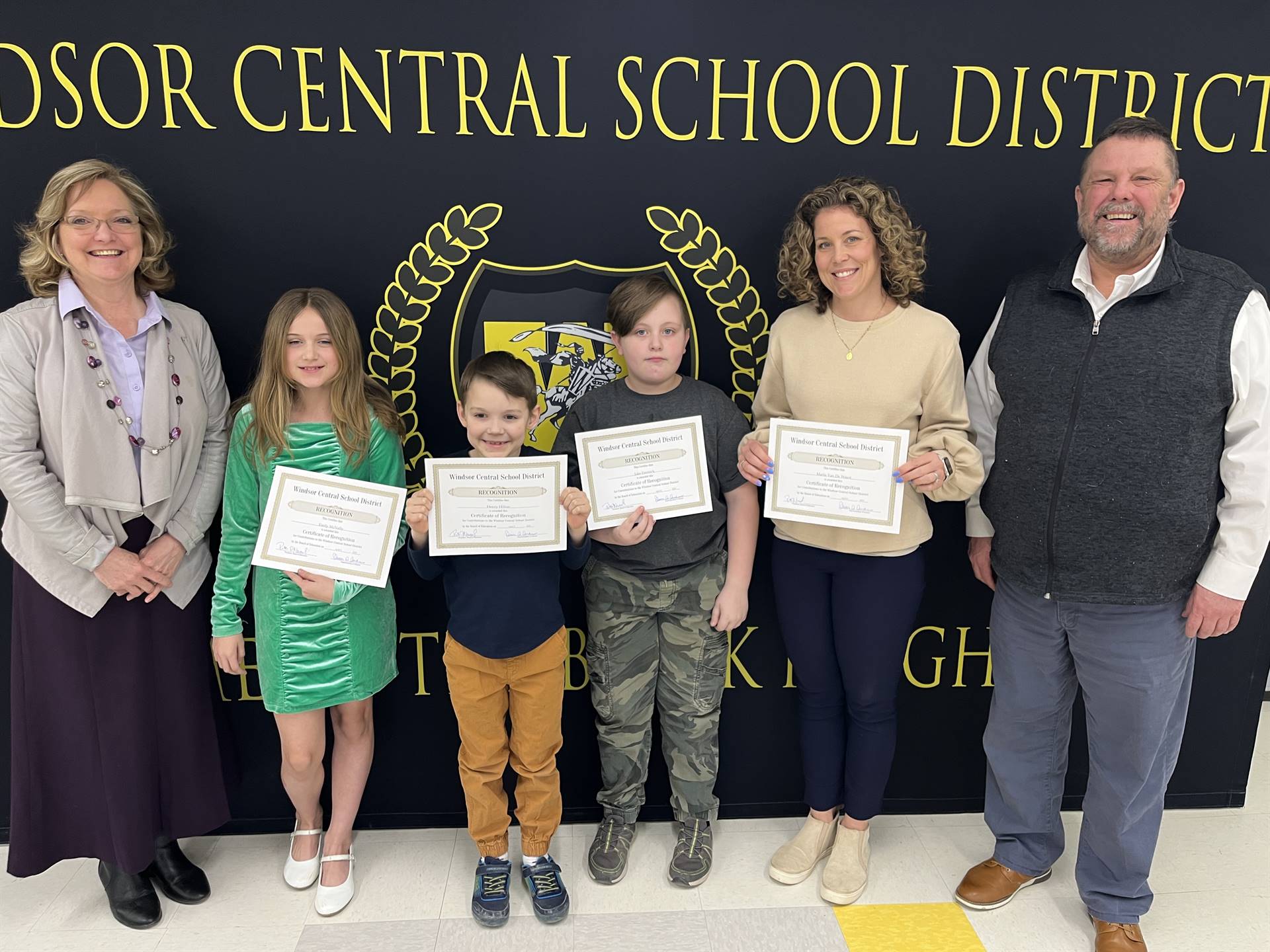 Three children standing between two women and a man in front of a banner