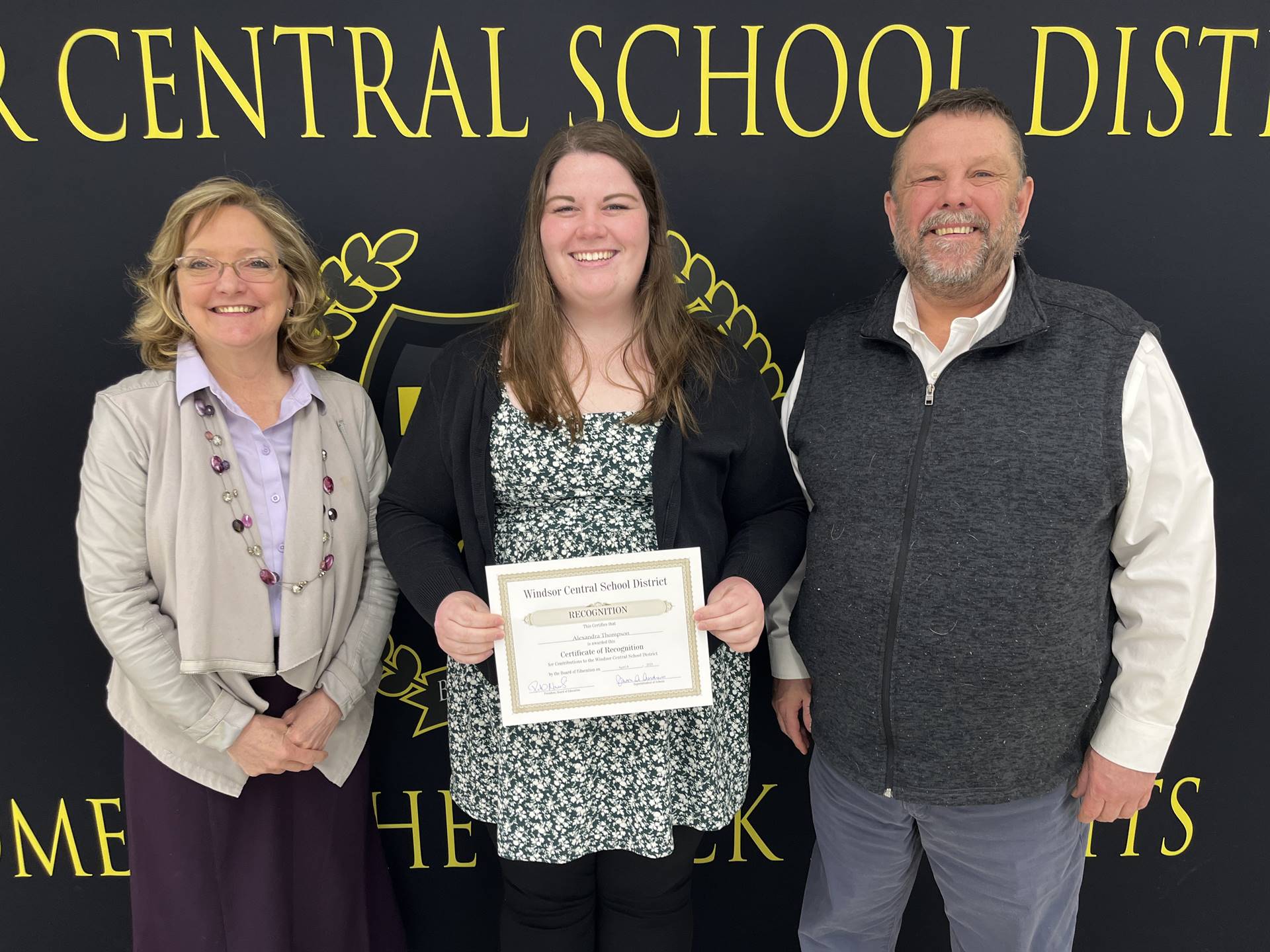 Margo Kibbler, Alexandra Thompson, and Pete Nowacki in front of a banner