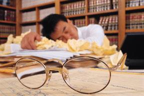 A man sleeping on a pile of papers with a pair of glasses in the foreground. 