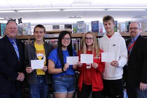 Four students hold certificates as two men look on