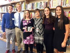 two boys and two girls stand with two women. One woman is holding an award.