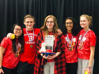 Five students stand together and one holds a trophy 