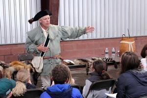 a man in colonial clothes speaks with children