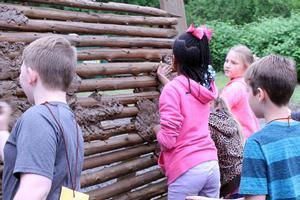 children smooth mud on a wall of logs