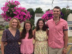 Three young women and one young man stand together with their arms around each other