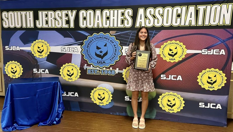 Scholar Athlete, Cadence anderson standing in front of giant banner for south jersey coaches association holding a plaque