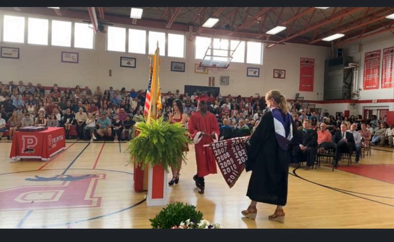 hs gym filled to capacity for graduation with principal & student president at center court with class banner