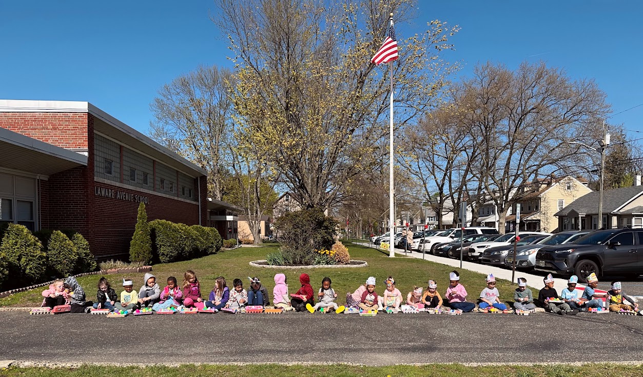 group of preschoolers seated on a curb viewing their plastic eggs from an egg hunt
