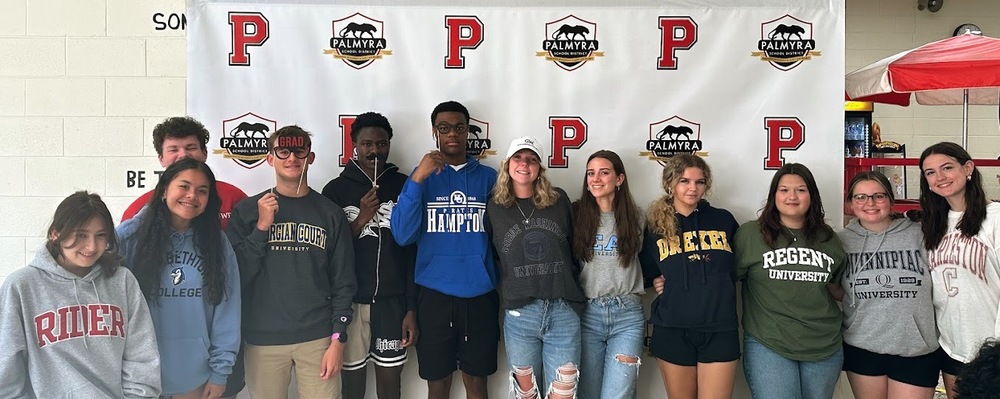 Group of students wearing college gear for photo in front of screen